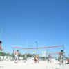 Spiaggia con persone che giocano a pallavolo sotto un cielo azzurro.