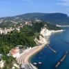 Veduta aerea di una costa con spiagge, scogli e città collinare.