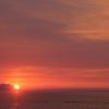 Tramonto rosato sul mare con isola all'orizzonte.