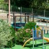 Area giochi all'aperto con scivolo giallo, rete per arrampicata e tavolo da ping pong.