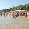 Turisti su una spiaggia affollata, alcuni in acqua, altri a riva.