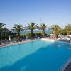 Una grande piscina circondata da palme e sedie a sdraio, con vista sul mare in lontananza.