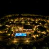 Vista aerea notturna di un complesso alberghiero con piscina illuminata e alberi attorno.