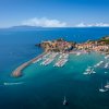 Porto turistico affacciato sul mare con barche ormeggiate e un borgo sulla costa.