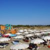 Spiaggia estiva con lettini e ombrelloni bianchi, più un grande gonfiabile a forma di nave.