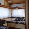 Tavolo e panchette in un camper con finestre luminose e tendine bianche.