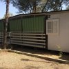 Una casetta bianca con tetto piatto, persiane e tende verdi, situata tra alberi.