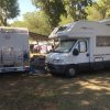 Due camper parcheggiati sotto gli alberi, con una veranda aperta e sedie all'esterno.