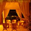 Gazebo illuminato con sedie di vimini, circondato da vegetazione.