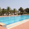 Piscina con palme, lettini bianchi e alberi sullo sfondo.