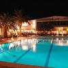Piscina illuminata di notte con palme e un edificio sullo sfondo.
