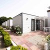 Bungalow moderno con terrazza, circondato da piante e fiori lungo un percorso pavimentato.
