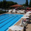 Piscina lunga con corsie, circondata da lettini e ombrelloni bianchi, alberi vicini.