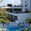 Piscina affollata accanto a un edificio moderno e piante.