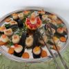 Vassoio con cozze ripiene su letto di rucola e carote, al centro decorazione vegetale.