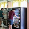 Due persone usano distributori automatici in una stanza luminosa con sedie e tavoli.