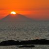 Tramonto sul mare con sole dietro un'isola.