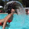 Persona in costume rosso solleva i capelli creando un arcobaleno d'acqua in piscina.