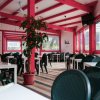 Sala da pranzo interna con tavoli e sedie nere, pareti rosse e grandi finestre.