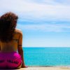 Donna seduta su un muretto, guarda il mare indossando pantaloncini rosa.