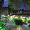 Giardino di sera con vialetti illuminati, alberi e gazebi.
