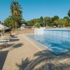 Una piscina con lettini bianchi e ombrelloni, circondata da palme.