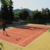 Campo da tennis all'aperto con due persone che giocano, circondato da alberi e colline.