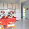 Cucina con tavolo apparecchiato, sedie rosse, e mobili bianchi. Finestra aperta sul giardino.