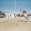 Persone giocano a beach tennis sulla sabbia, attorno a una rete.