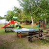Area giochi con scivoli e tavolo da ping pong, circondata da alberi e staccionate di legno.