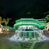 Edificio moderno illuminato di verde di notte, situato tra rocce e palme.