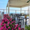 Terrazza con tavoli e sedie, decorata con fiori rosa vivaci, vista sul mare in lontananza.