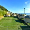 Campo da tennis in erba, circondato da strutture rotonde e vegetazione con vista mare.