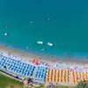 Spiaggia affollata vista dall'alto, con ombrelloni gialli e blu vicino al mare turchese.