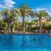 Piscina all'aperto con persone che nuotano e si rilassano, circondata da palme.