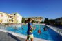 Ragazzi giocano in piscina, circondata da edifici gialli e cielo sereno.