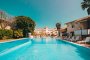 Una piscina lunga tra edifici bianchi e alberi.