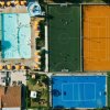 Vista aerea di una piscina, un campo da calcetto e due campi da tennis con ombrelloni gialli.