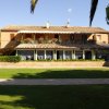 Una casa colonica a due piani con veranda e balcone, circondata da un prato e alberi.