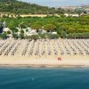 Una spiaggia affollata con file di ombrelloni e folta vegetazione alle spalle.