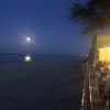 Una spiaggia di sera con luna piena e tavoli all’aperto illuminati.