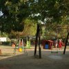 Un parco giochi all'aperto con altalene, casetta rossa e verde e scivolo, circondato da alberi.