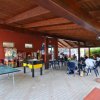 Un'area coperta con tavolini, sedie, calcio balilla e ping-pong, persone sedute e giochi.