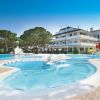 Una piscina con fontane, scivoli gialli e un edificio bianco sullo sfondo, circondato da alberi.